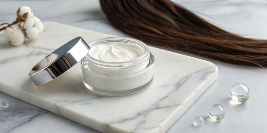 Hair strengthening cream treatment in a jar next to a single strand of hair.